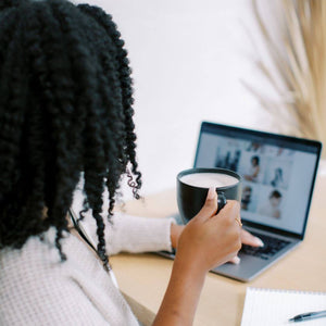 A woman with curly hair holds a mug while browsing on her laptop, exploring wellness resources or support services through Hem's Pelvic Health Resources.